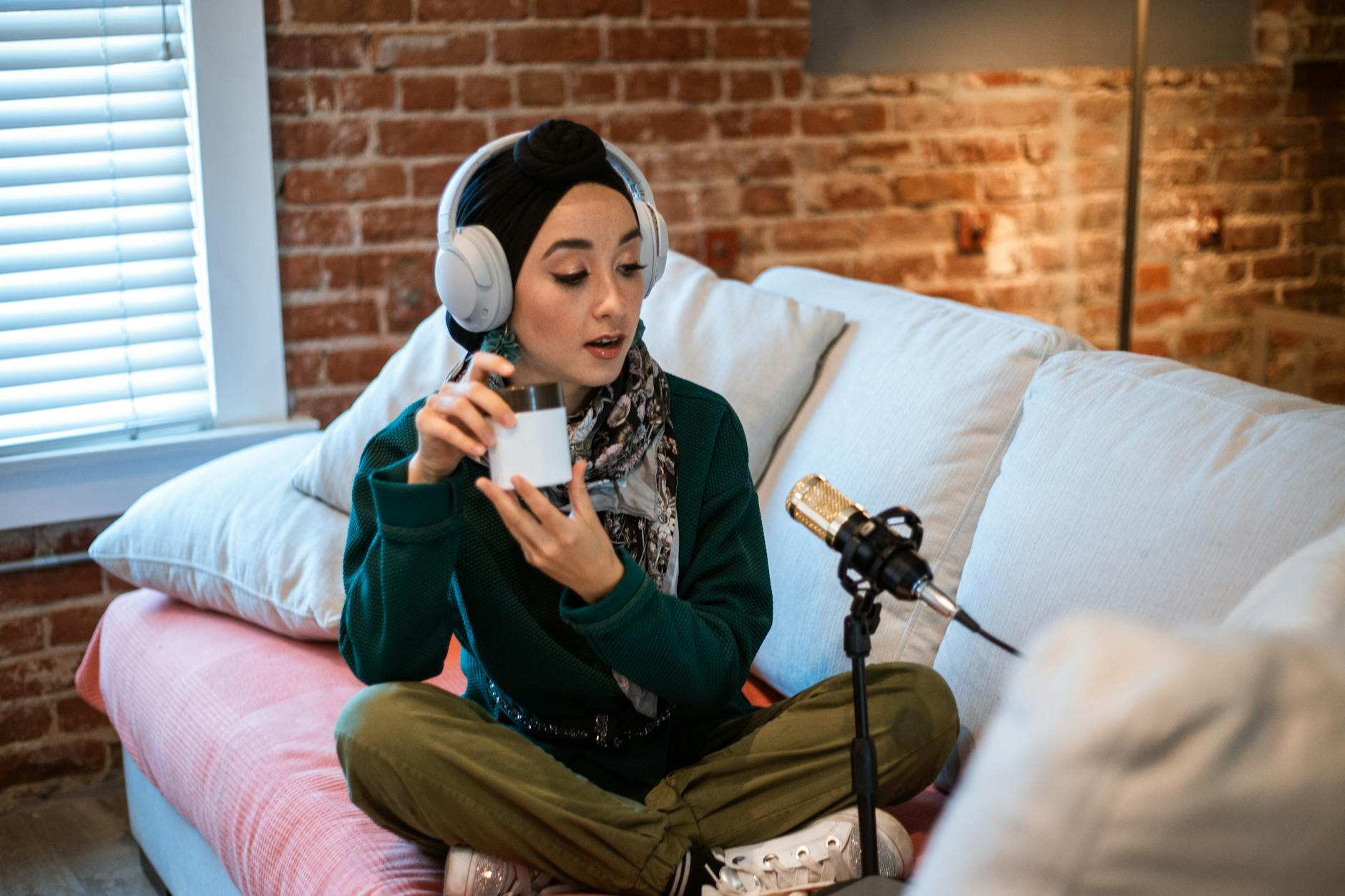 Woman in Green Long Sleeve Shirt and Green Pants Sitting on Sofa Holding a Beauty Product